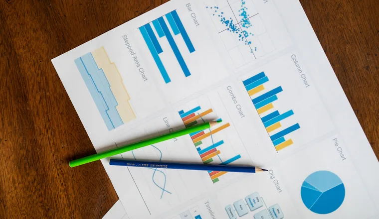 Printed bar and pie charts on a sheet of paper with two coloured pencils resting on a wooden desk.