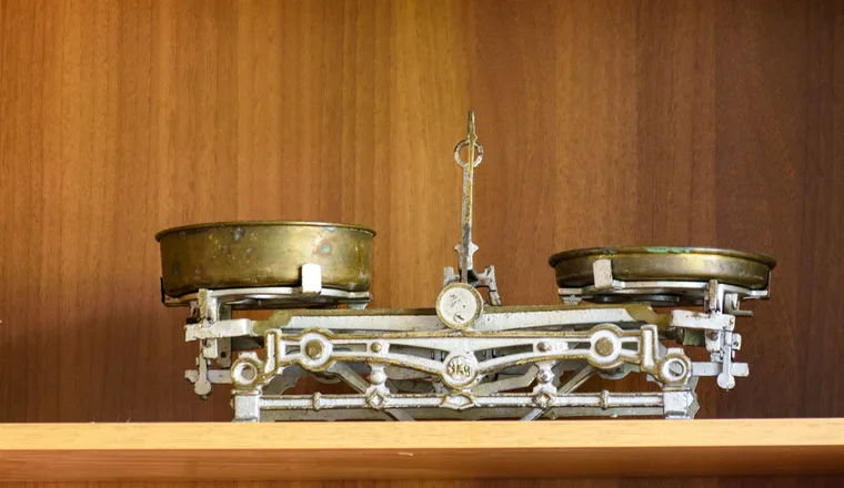 An old balance scale with two brass pans standing on a wooden shelf.