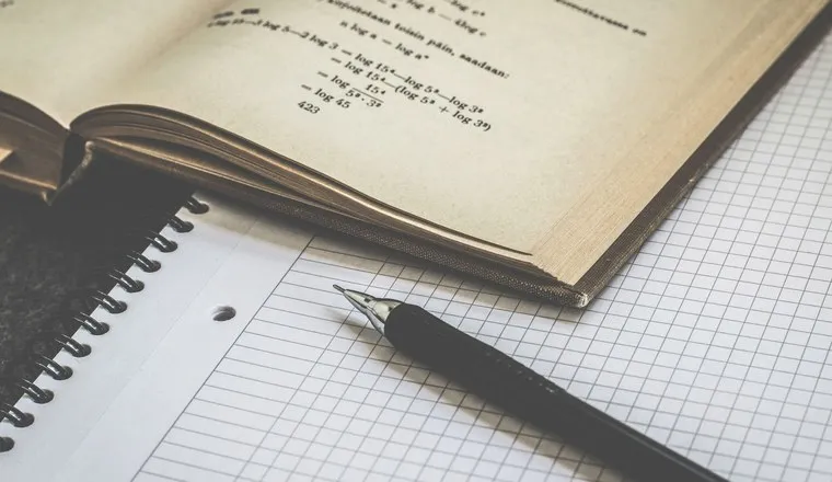 An open notebook of handwritten calculations with a pen resting on it