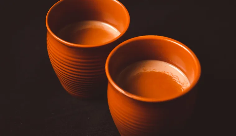 Two clay cups of tea side by side on a dark table.