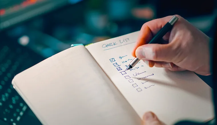 A hand ticking boxes on a handwritten checklist in an open notebook.