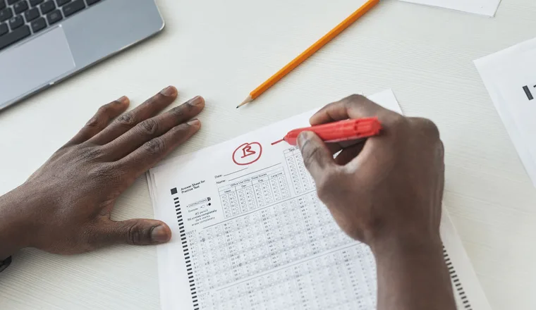 A hand checking a stack of exam papers with a red pen