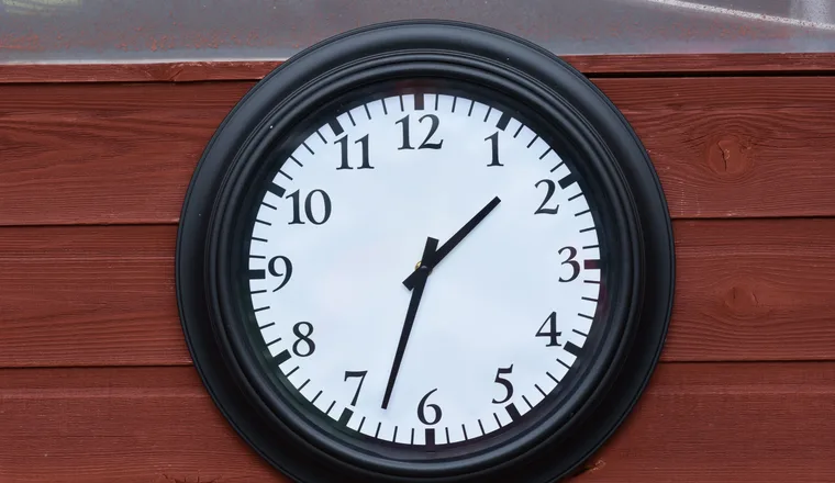 A round black wall clock with a white face hanging on a wooden wall.