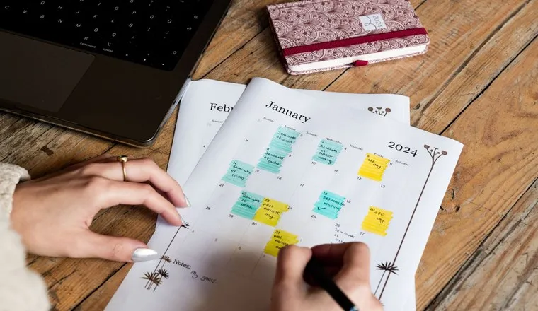 Hands annotating a monthly planner with coloured sticky notes