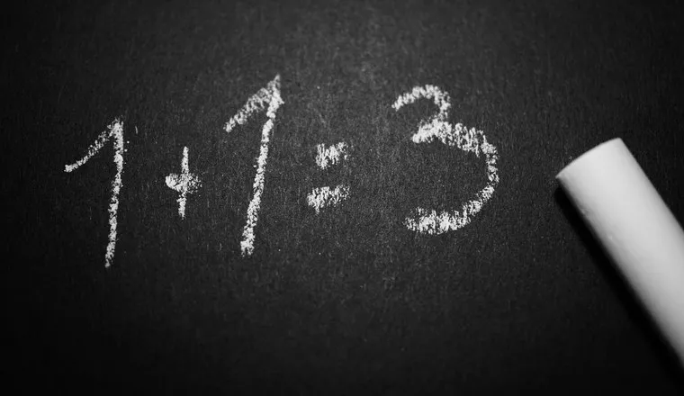 The sum 1 + 1 = 3 chalked on a blackboard beside the chalk