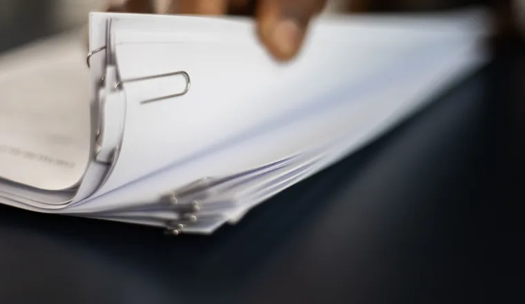 A clipped bundle of papers being lifted from a stack by one hand