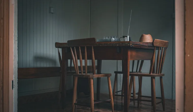 A wooden table with a few empty chairs drawn up to it in a quiet room