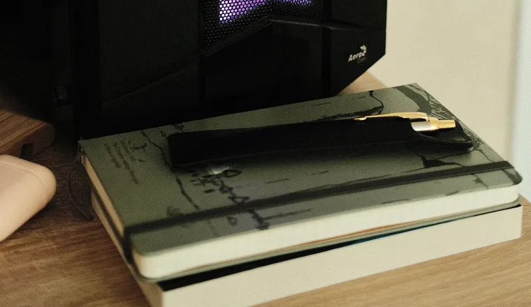 A stack of notebooks and a pen under the glow of a desk lamp