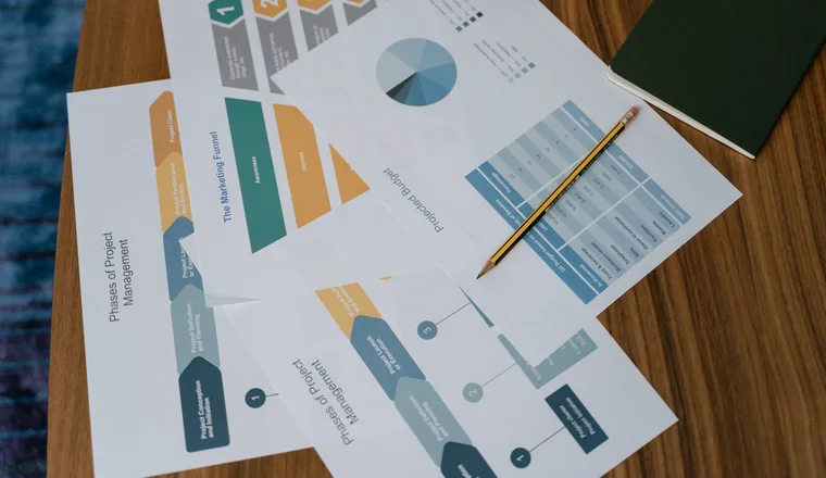 Printed charts and documents spread across a desk with a pencil