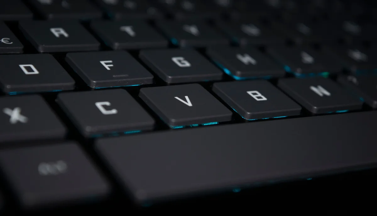 A laptop keyboard lit low, an open notebook beside it